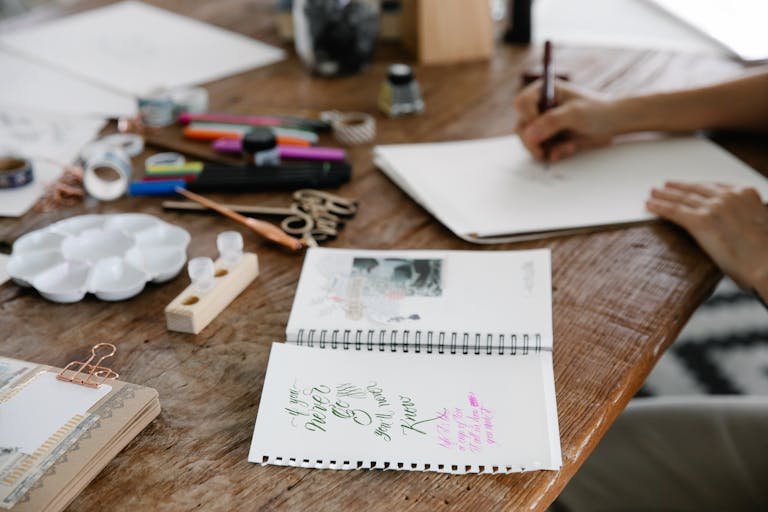 A wooden table filled with art supplies and sketches, showcasing creative work in progress.