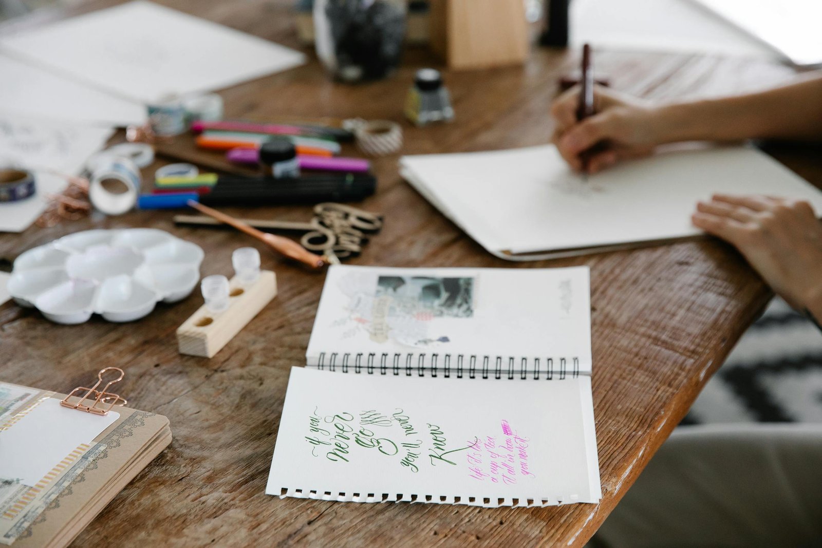 A wooden table filled with art supplies and sketches, showcasing creative work in progress.